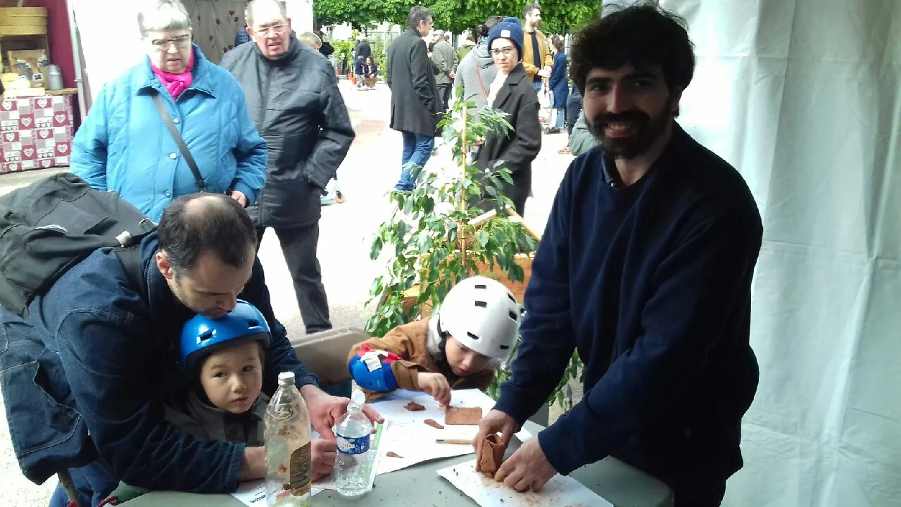 Des enfants et des adultes travaillent l’argile autour d’une table et de petits pots.